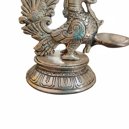 Detailed view of engraved circular base of antique brass peacock diya with petal and arch motifs