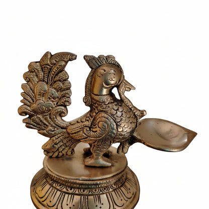 Close-up of antique brass peacock diya head with natural oxidised patina highlighting fine relief detailing