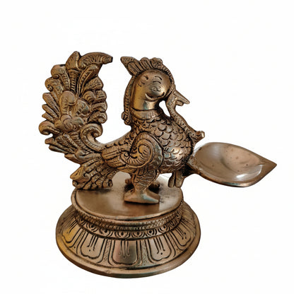 Side view of antique brass peacock oil lamp showing fanned tail feathers and detailed scale work with natural patina