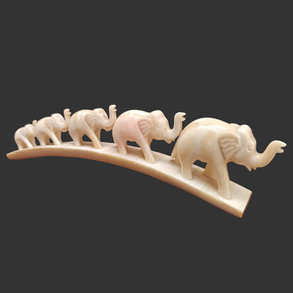 Carved bone elephant parade on arched base displayed on wooden surface – front view