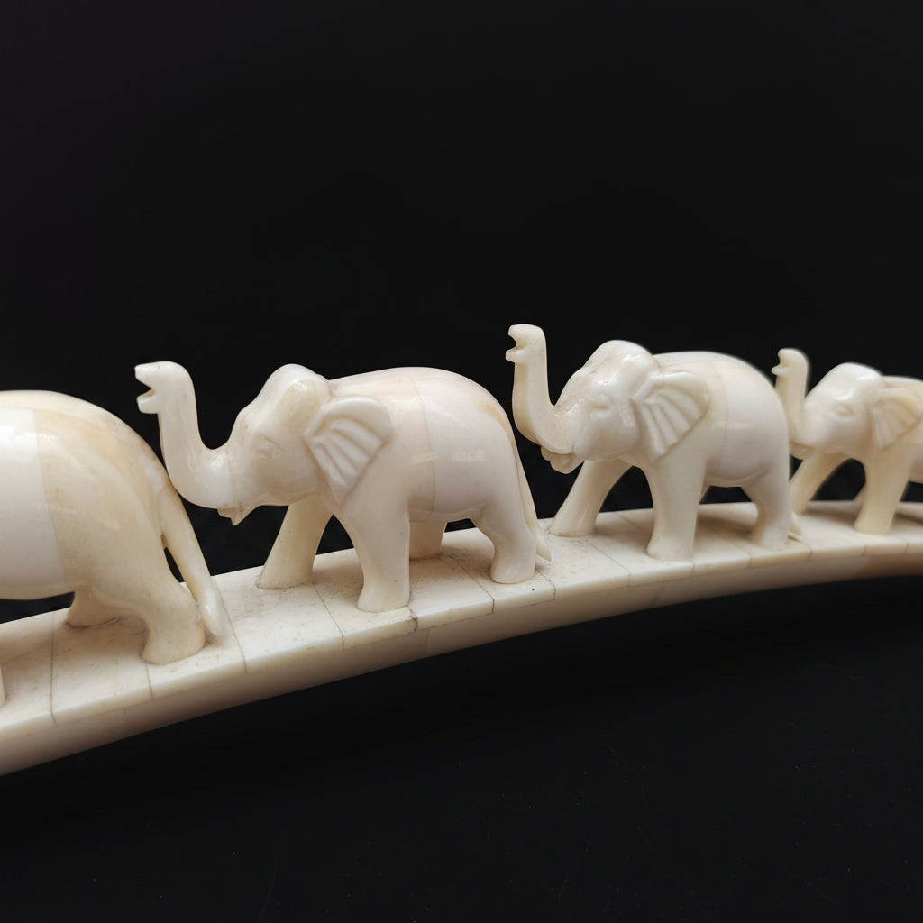 Close-up of carved bone elephants standing in a row on arched base