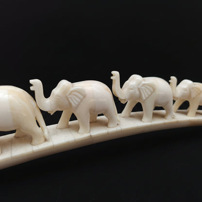 Close-up of carved bone elephants standing in a row on arched base