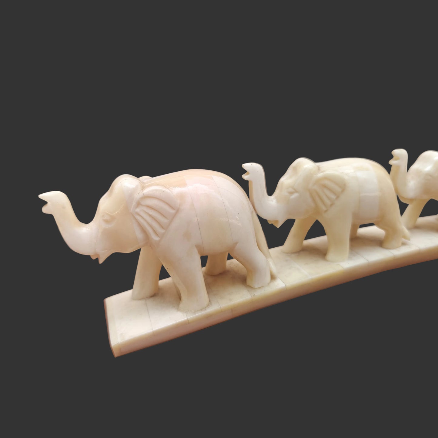 Close-up of carved bone elephants standing in a row on arched base