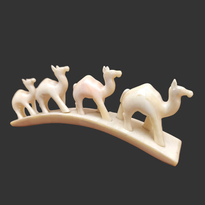 Carved bone four-camel parade on arched base displayed on wooden surface – front 