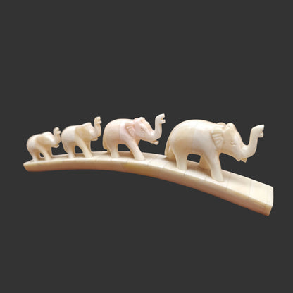 Carved bone four-elephant parade on arched base displayed on wooden surface – front view

