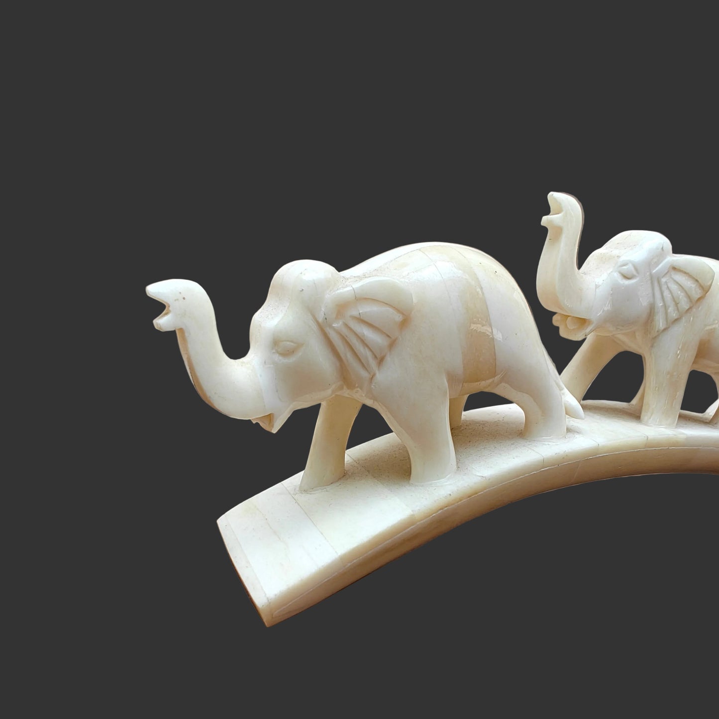 Carved bone three-elephant parade on arched base displayed on wooden surface – front view-1