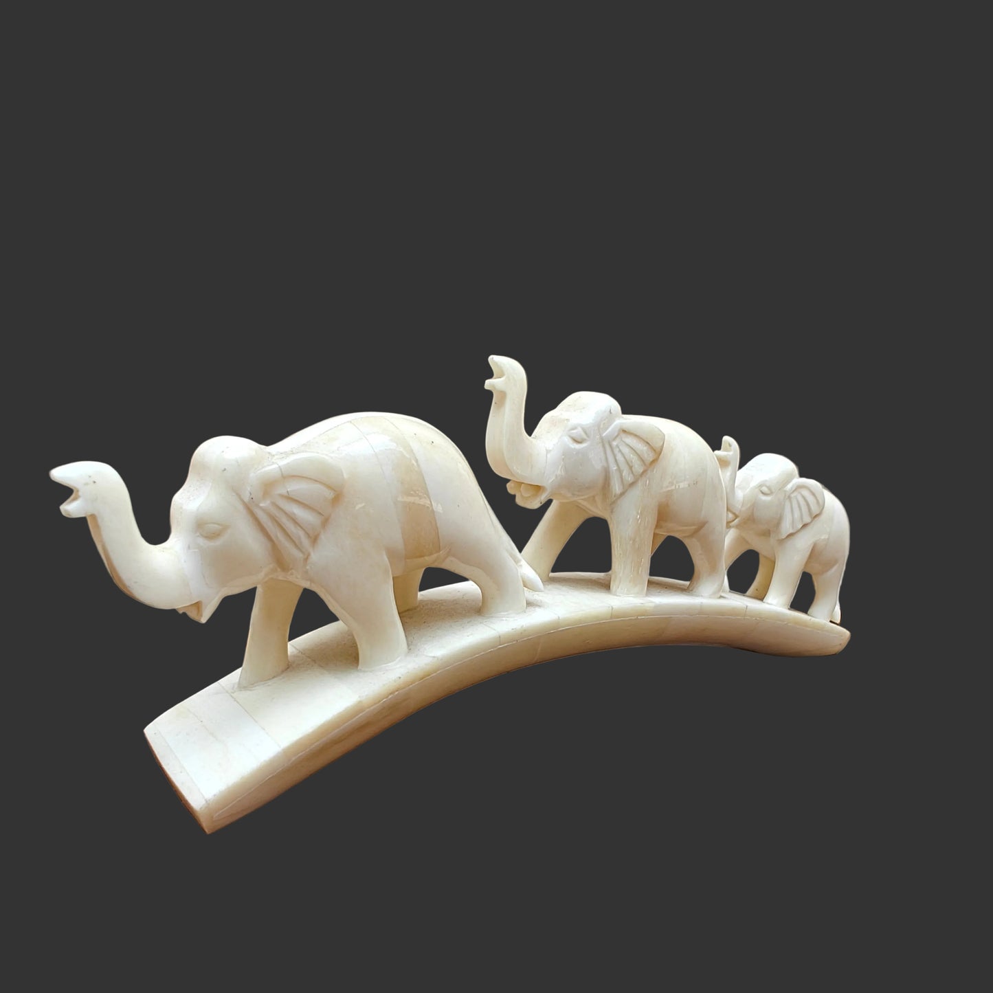 Carved bone three-elephant parade on arched base displayed on wooden surface – front view